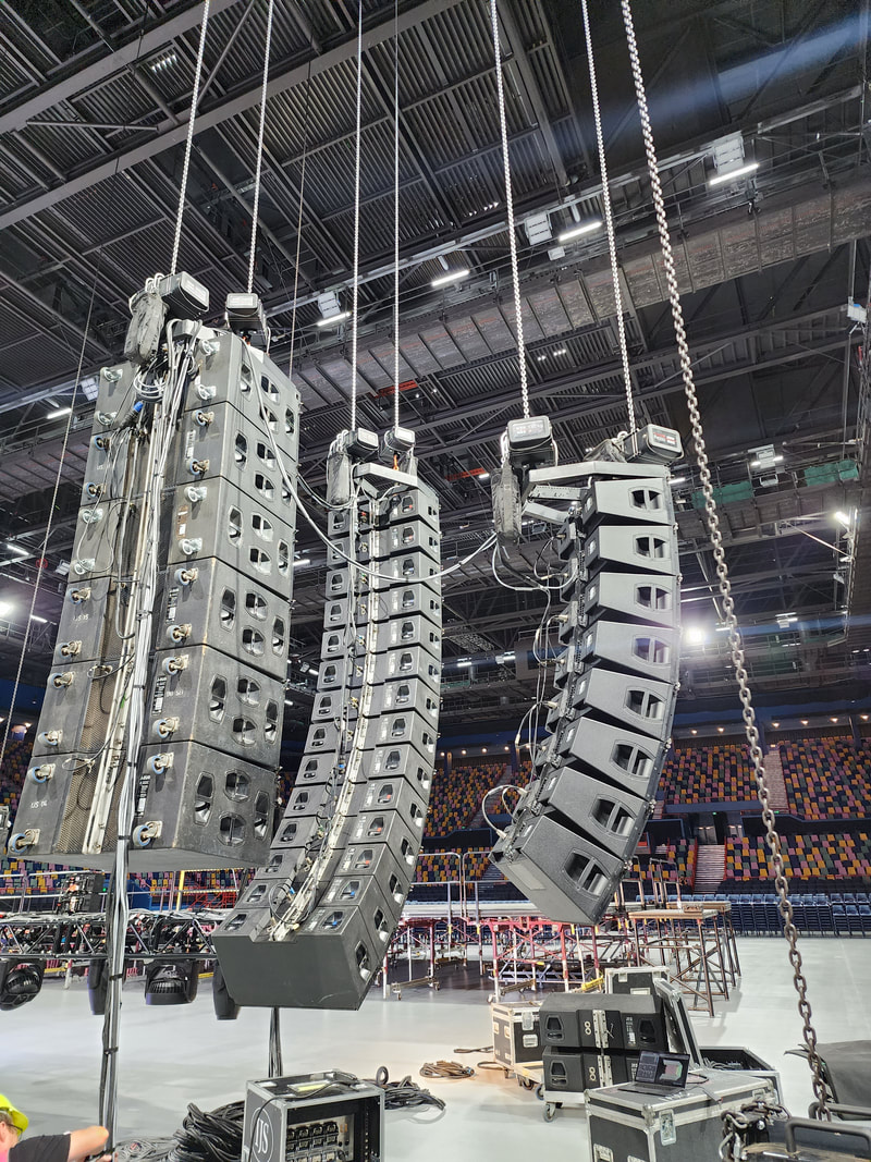 Line array speaker clusters being rigged in arena